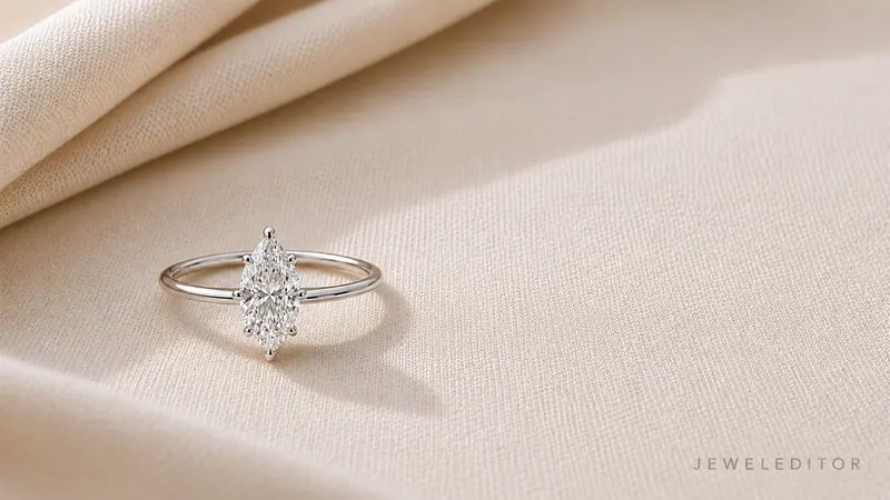 Marquise-cut diamond engagement ring in thin platinum solitaire on cream linen, photographed east-west, elongated shape with pointed tips.