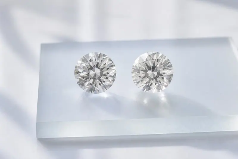 Two loose round diamonds side by side on clear acrylic