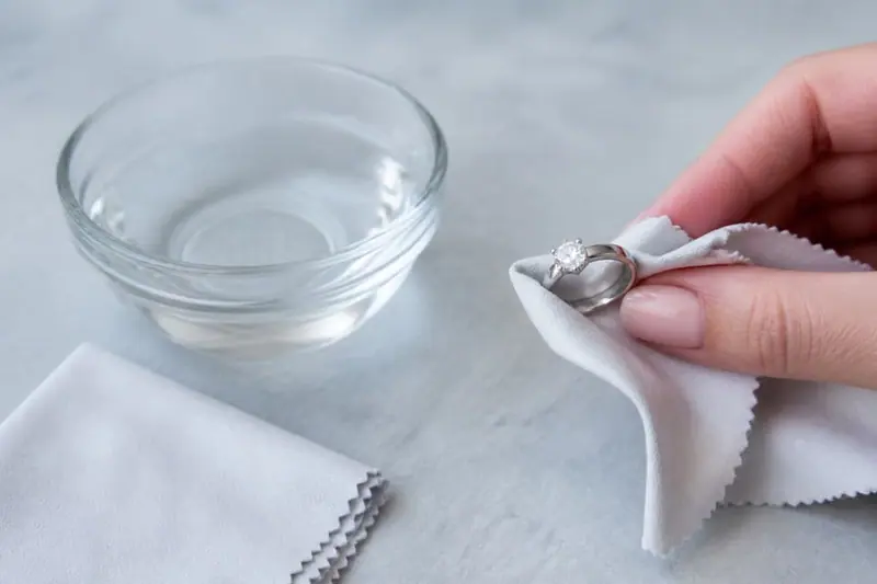 Cleaning an engagement ring with a soft cloth beside a glass bowl of water
