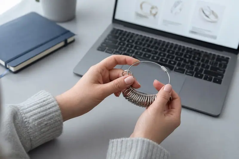 Hands holding a ring sizer beside a laptop showing rings