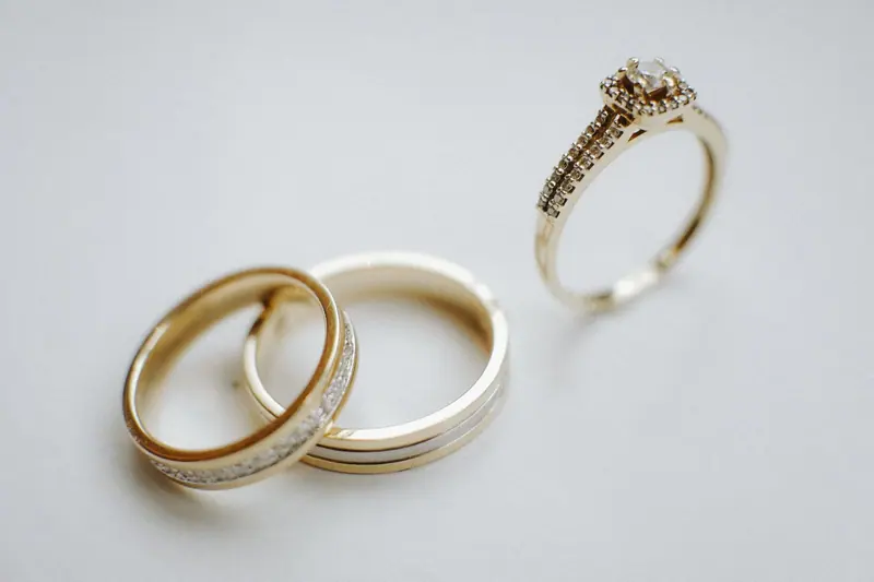 Two yellow gold wedding bands and a gold engagement ring on a white surface