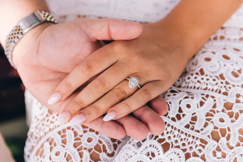 Pear-shaped halo engagement ring on a hand resting on white lace