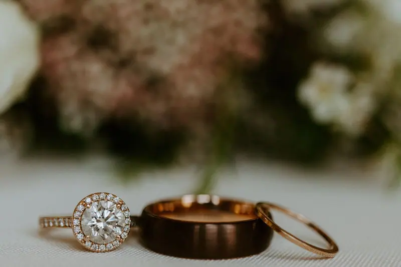 Halo engagement ring beside rose gold and dark wedding bands