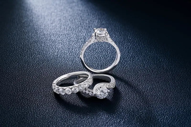 Diamond engagement ring and two diamond wedding bands on a navy surface