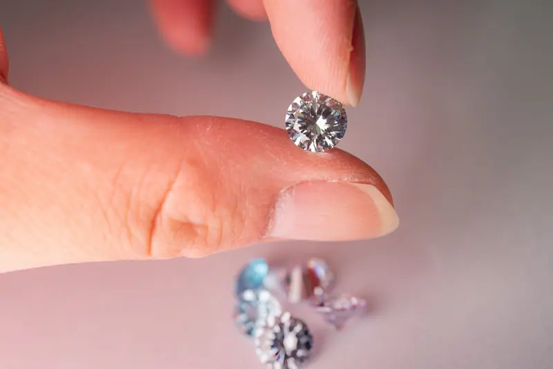 Fingertips holding a loose round diamond above smaller loose stones