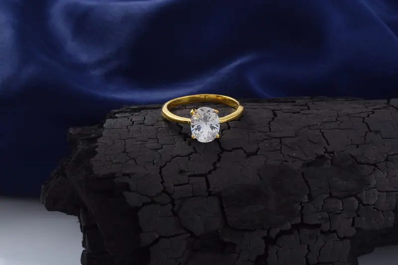 Oval diamond solitaire in yellow gold resting on dark stone