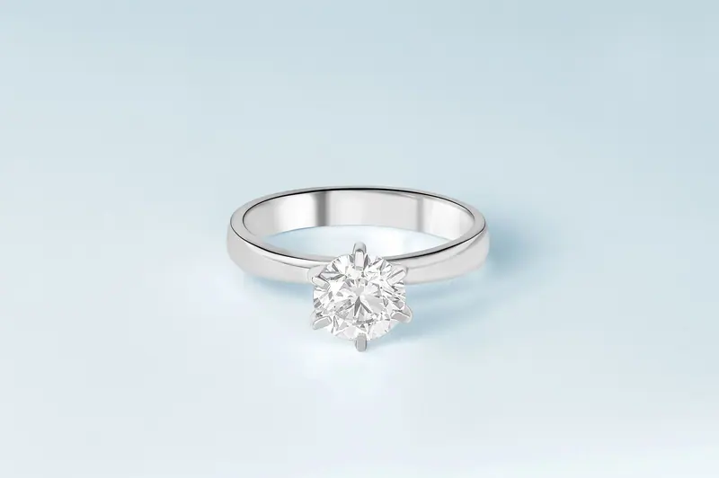 Six-prong solitaire engagement ring in white metal on a pale blue background