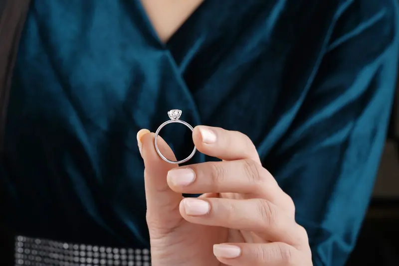 A woman holding a solitaire engagement ring between her fingers